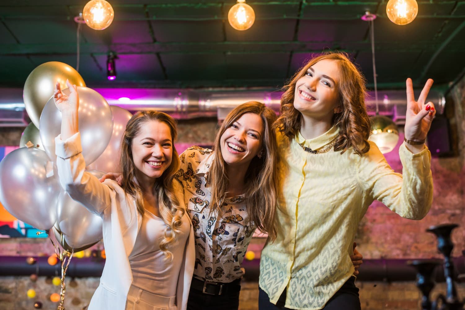 Three women posing with silver balloons, happy and festive mood.
