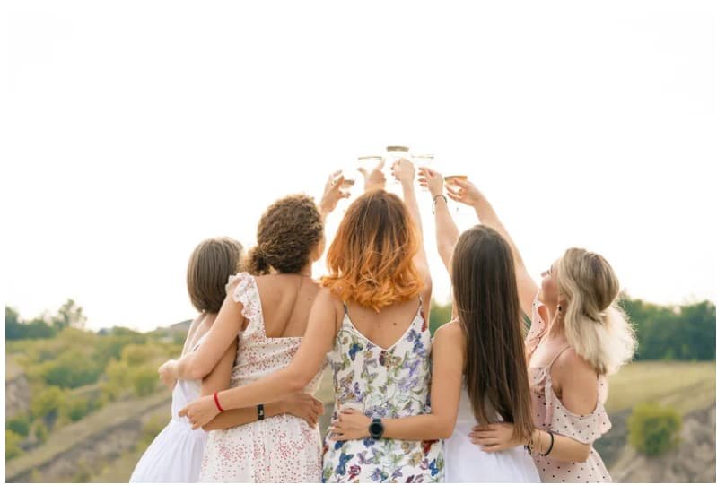 Women in summer dresses toasting outdoors, joyful celebration.