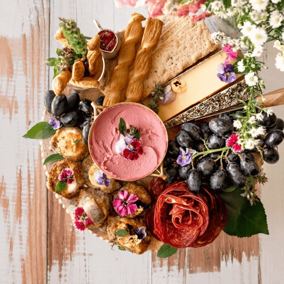 Charcuterie board with dip, salami, cheese, grapes, and edible flowers.