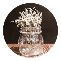 Glass jar with dried white flowers on wood table, rustic and cozy vibe.