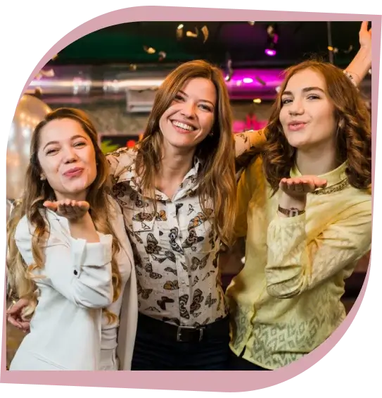 Three women indoors smiling and blowing kisses at a festive event.